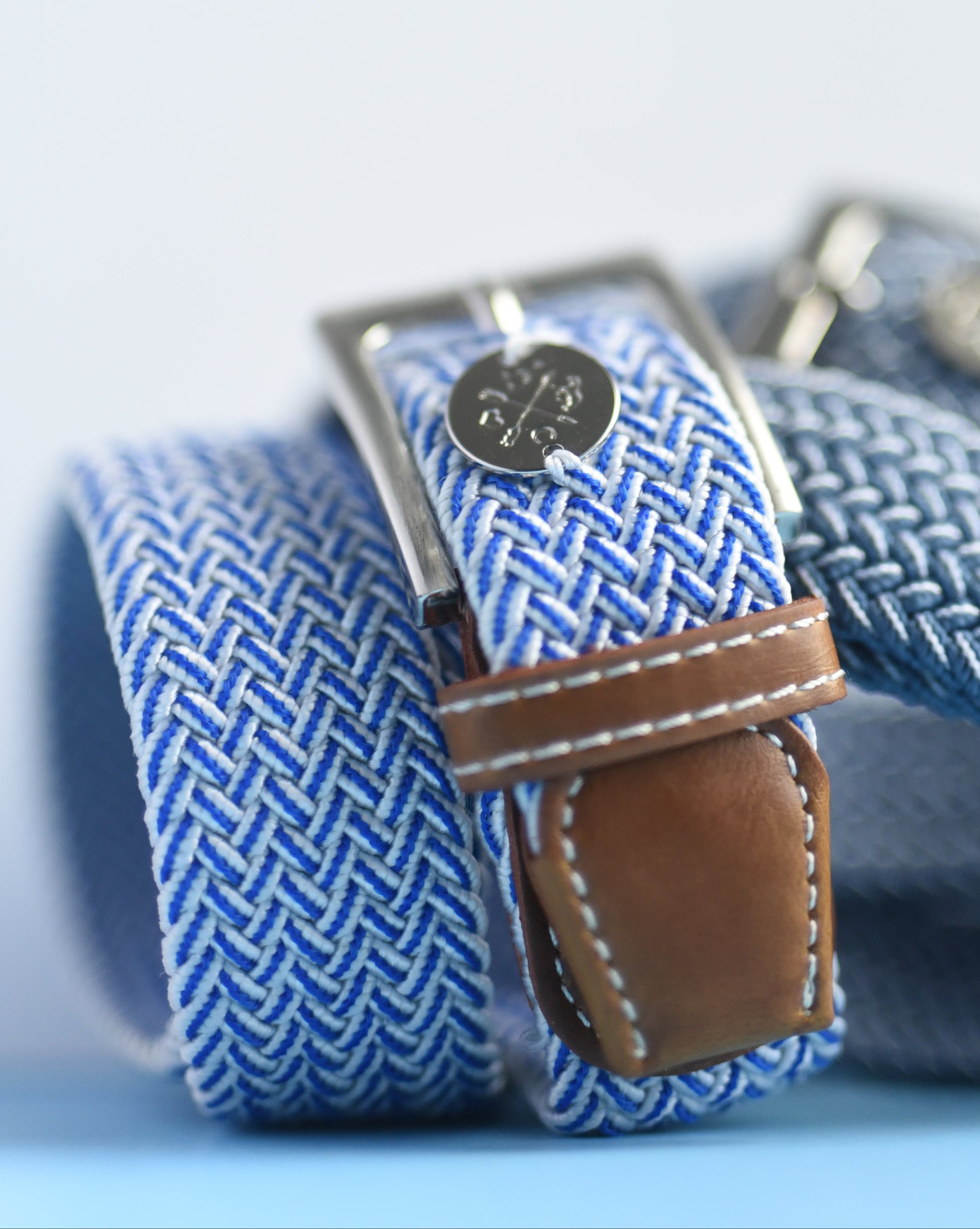 Blue woven belt with a brown leather strap on a light blue background